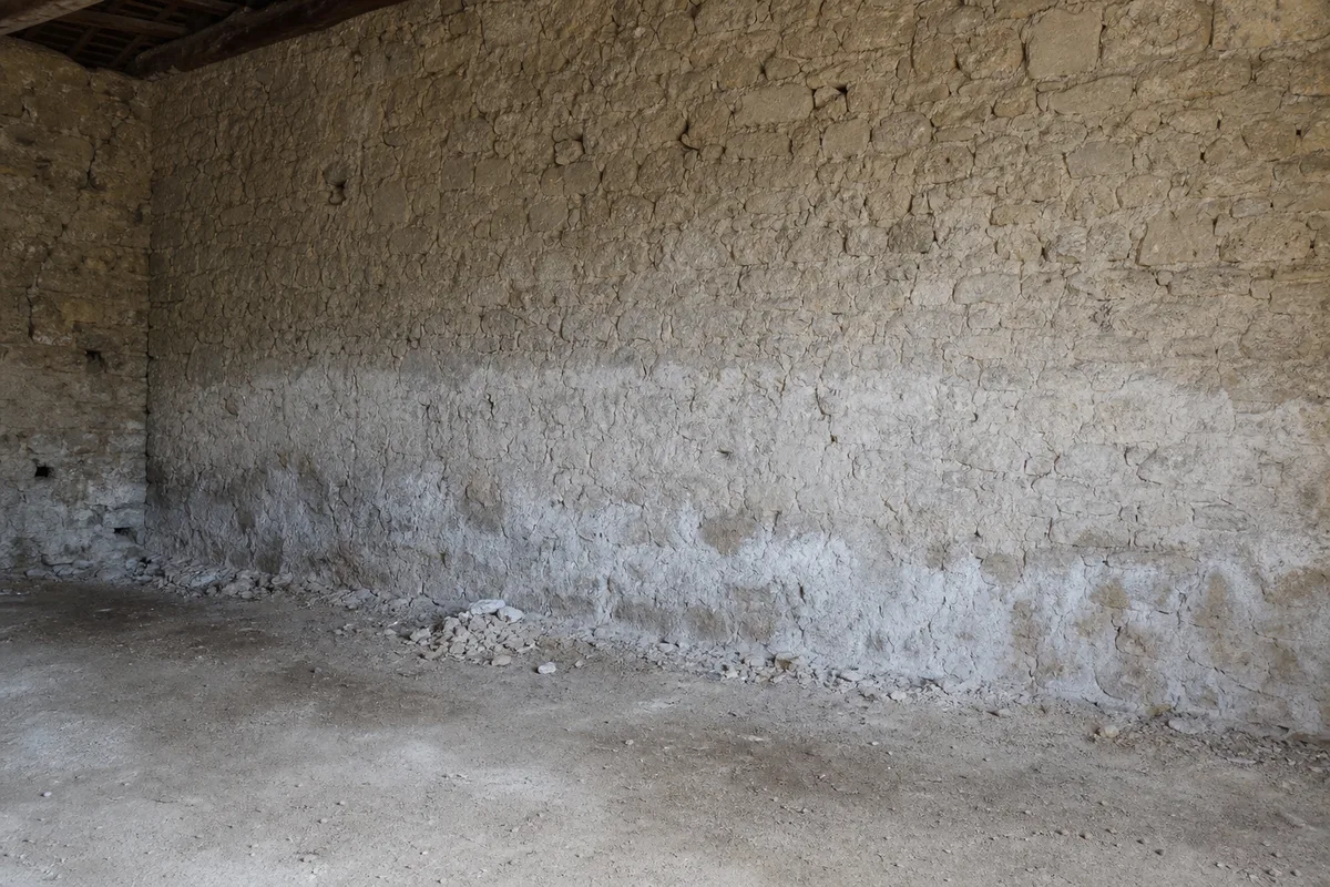 Mur en pierre décapé et nu, laissé au séchage dans une pièce vide en travaux